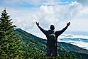 Man with arms raised relaxing on spring hiking trip. Man on top of the mountain enjoying beautiful foggy scenery. Mount Mitchell State Park, near Asheville, North Carolina