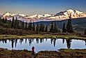 view of alaska's mount denali looms over calm pond at sunset, with clear blue sky above