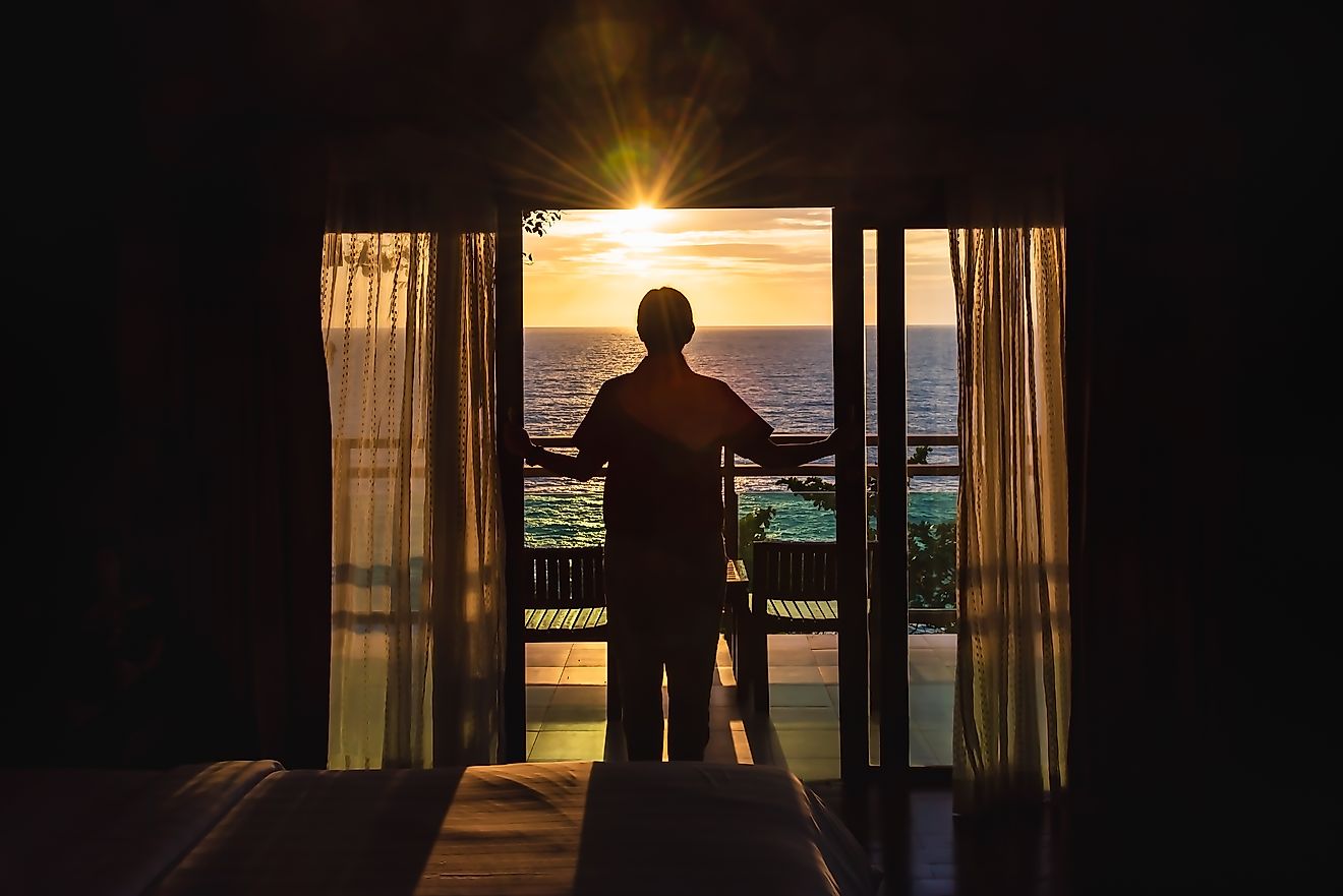 Woman open the door to see ocean sunrise view from bedroom balcony for travel concept.