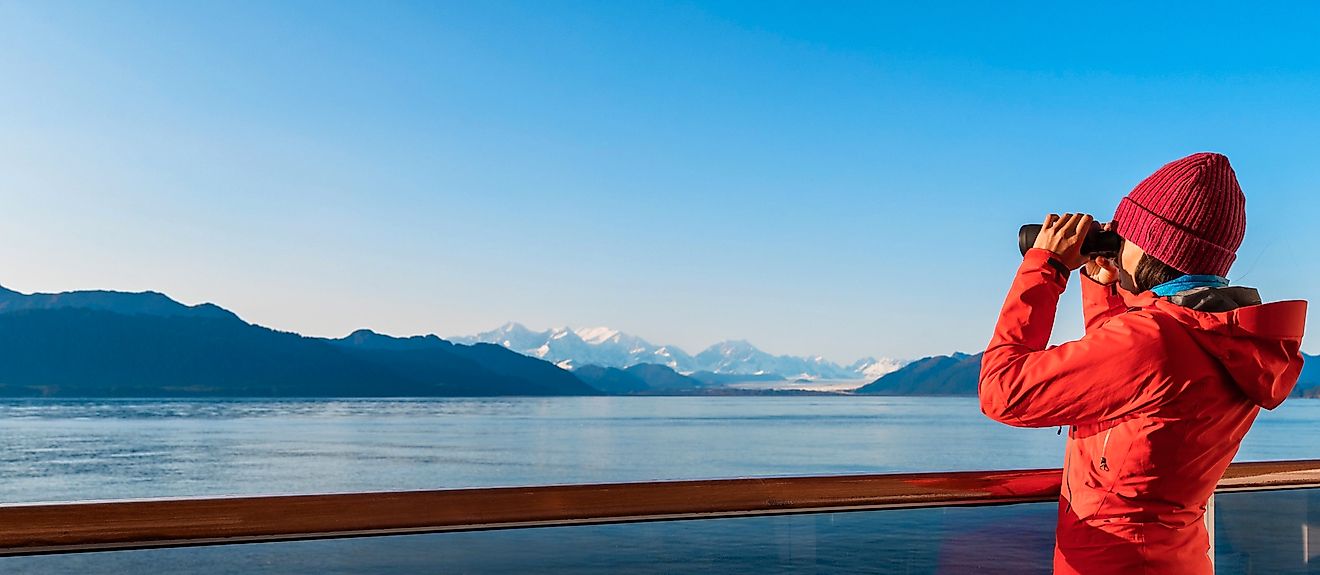 Alaska Glacier Bay cruise ship passenger looking at Alaskan mountains in binoculars exploring Glacier Bay National Park