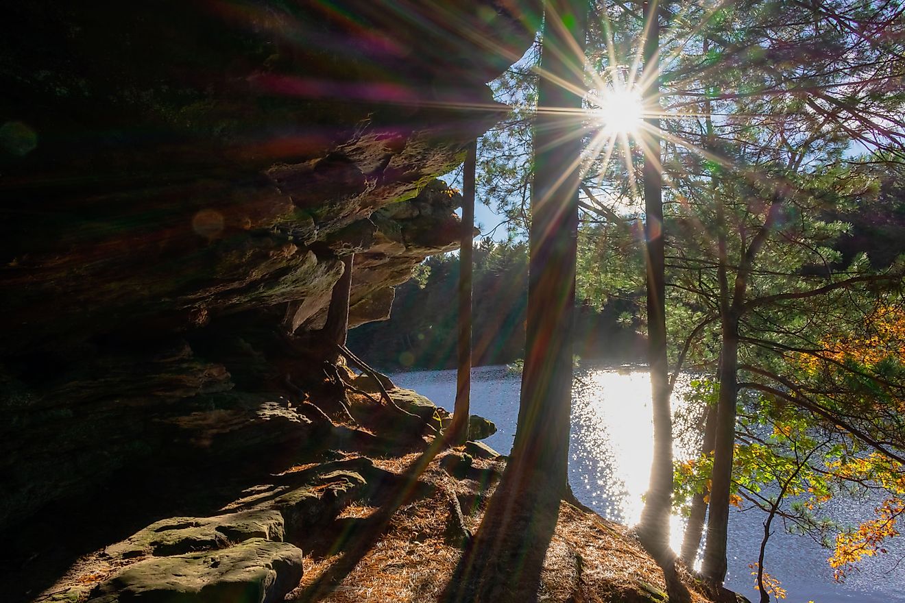 Sun beams sparkling on lake and shining through trees along sandstone bluff