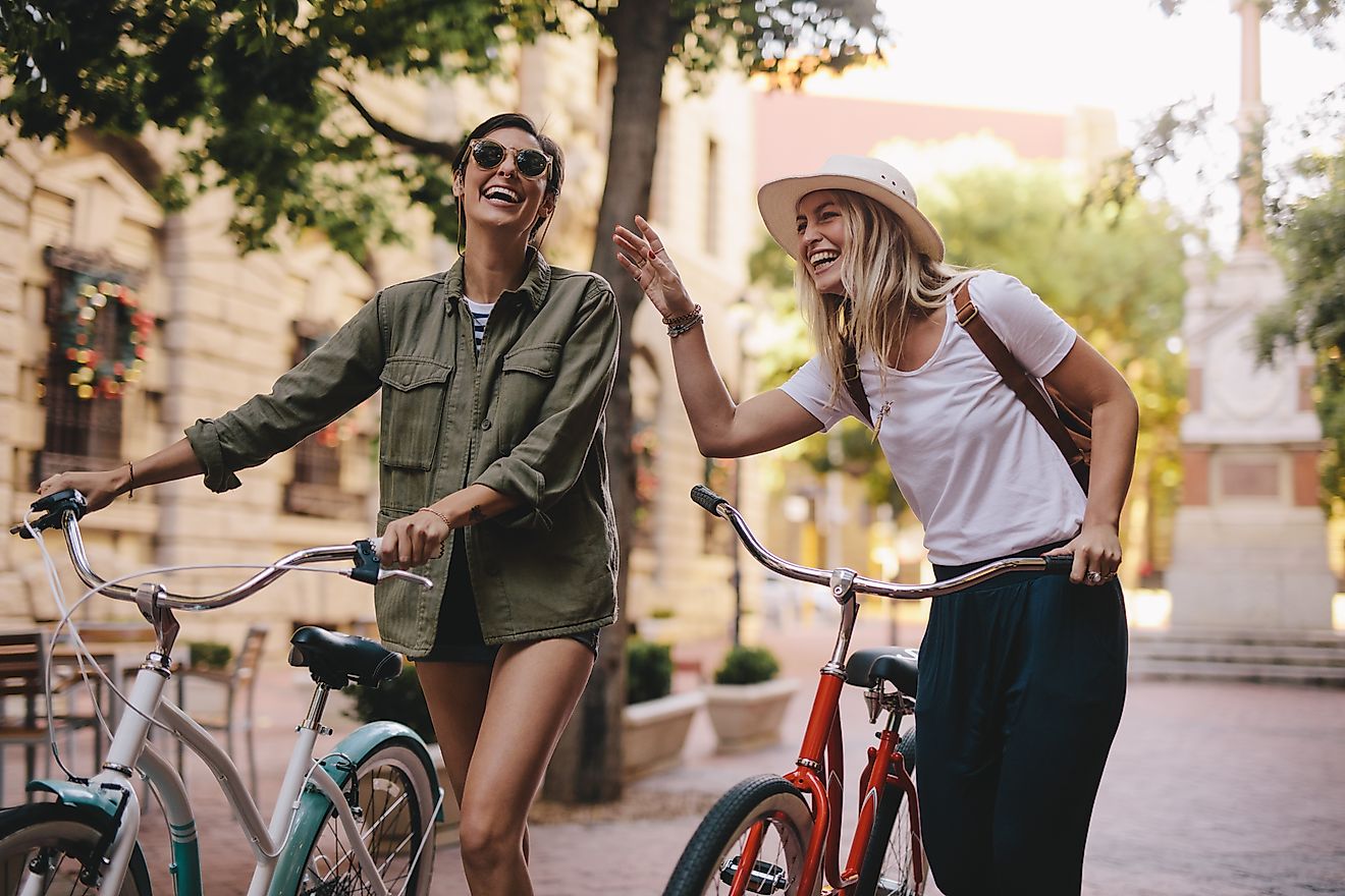 Positive and happy girls walking on the city street with bicycles