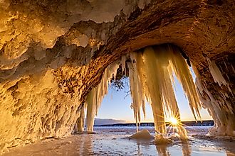 Lake Superior Ice Cave at Sunrise. The sun crests the horizon and shines through hanging ice curtains as it rises and illuminates the interior of a cave on Grand Island in Michigans Upper Peninsula.