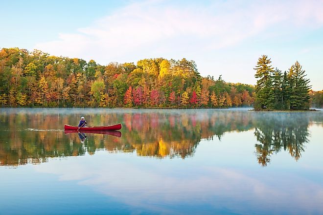 Senior man paddling a red wooden canoe on a beautiful northern Minnesota lake 