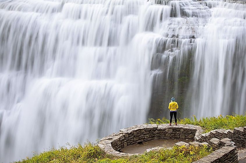 Solo female hiker stands near the edge of a cliff overlooking a giant waterfall. Letchworth State Park, upstate New York