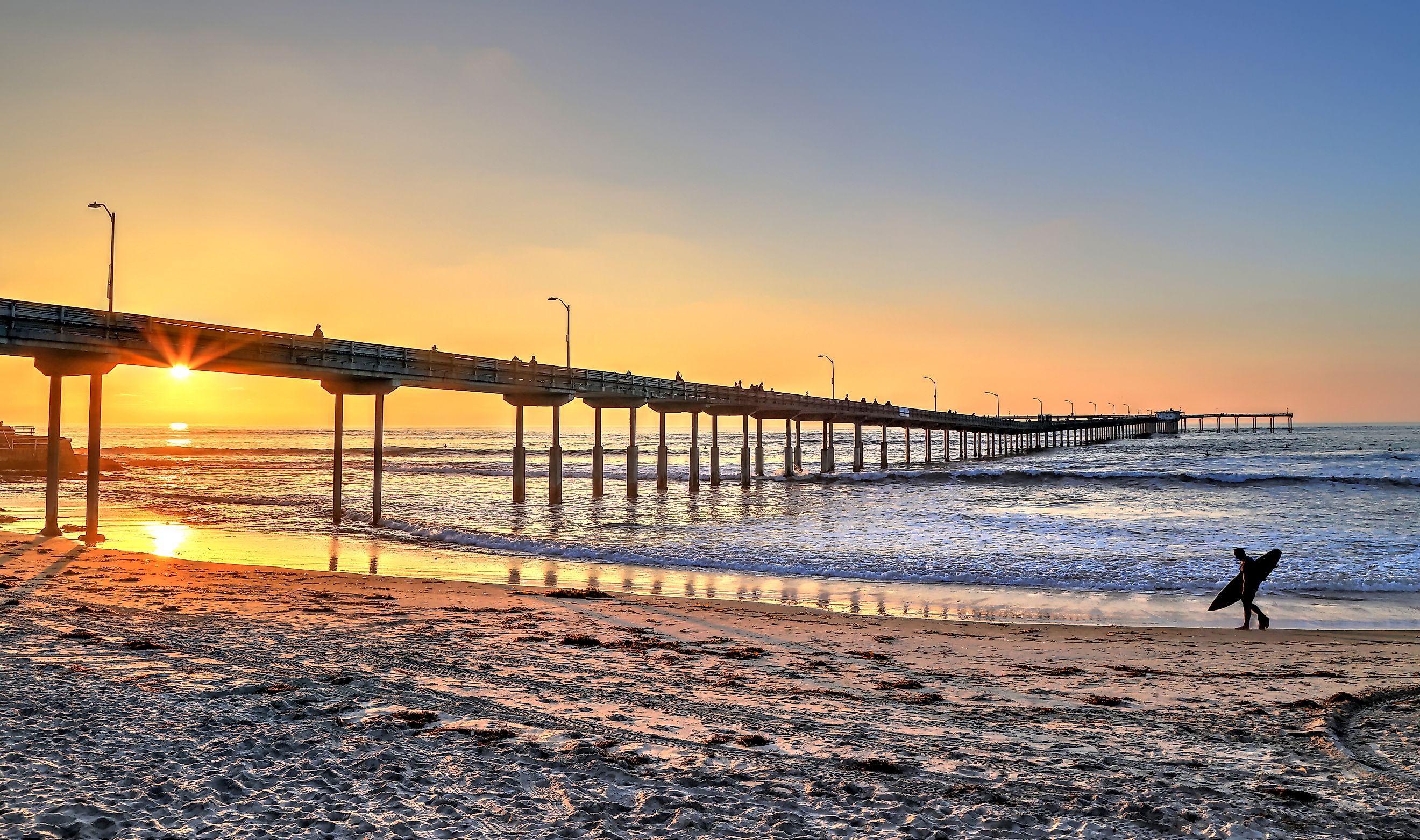 A surfer walks on Ocean Beach near the pier in San Diego, California.