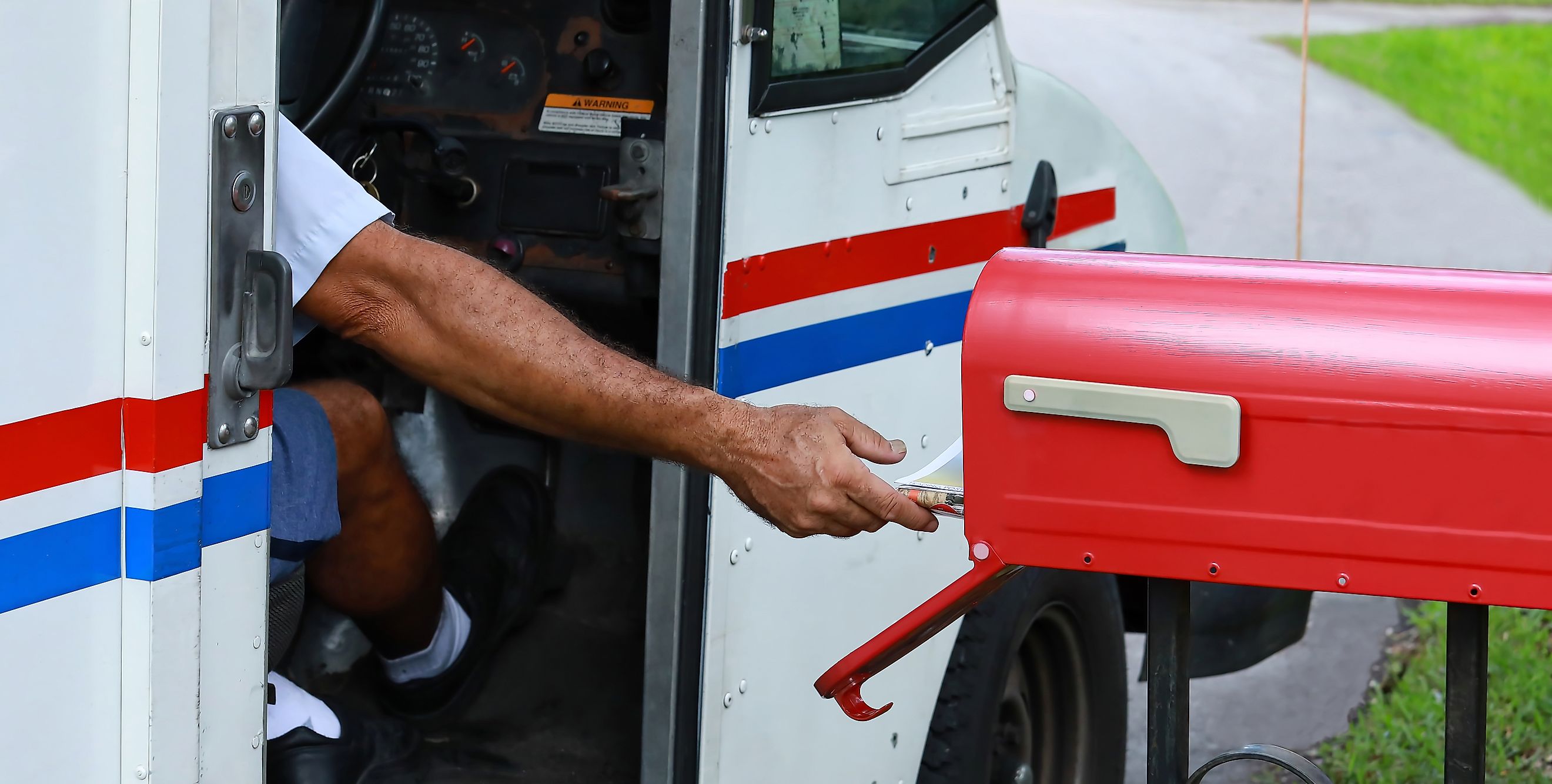 : Mail man reaches out of his truck to deliver mail.