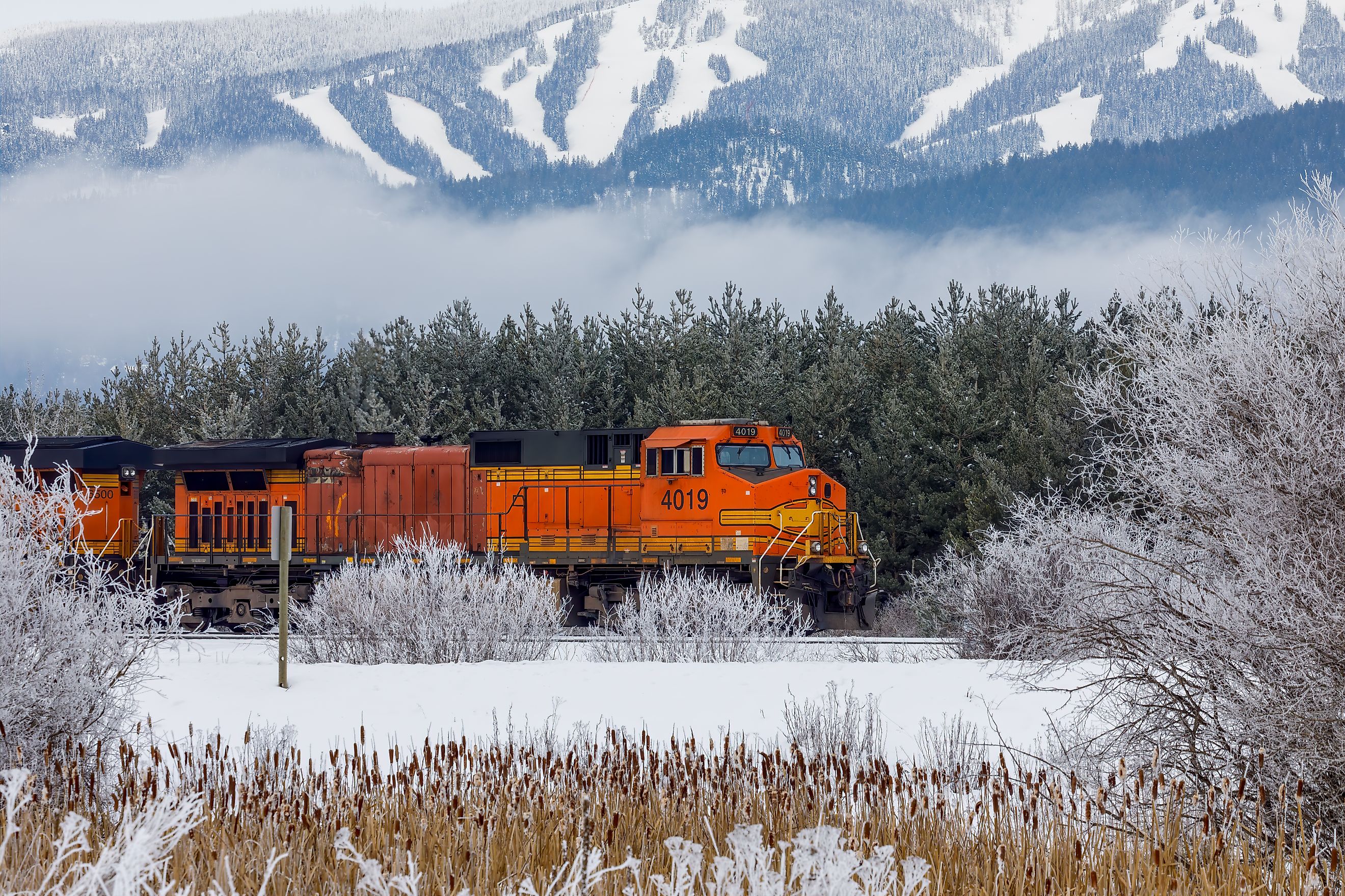 locomotive pulling train in winter close to Whitefish, Montana with Whitefish ski resort in background