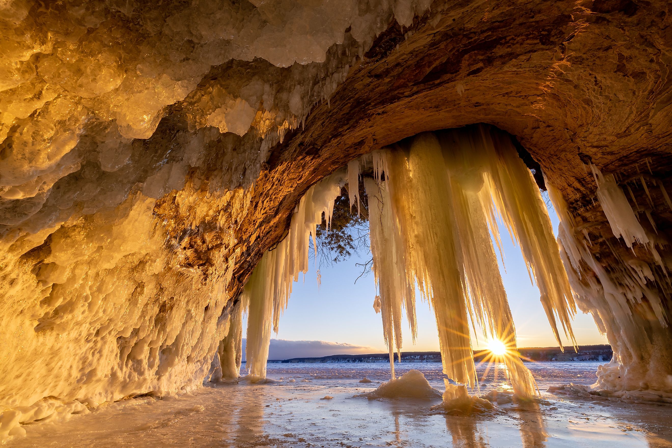 Lake Superior Ice Cave at Sunrise. The sun crests the horizon and shines through hanging ice curtains as it rises and illuminates the interior of a cave on Grand Island in Michigans Upper Peninsula.