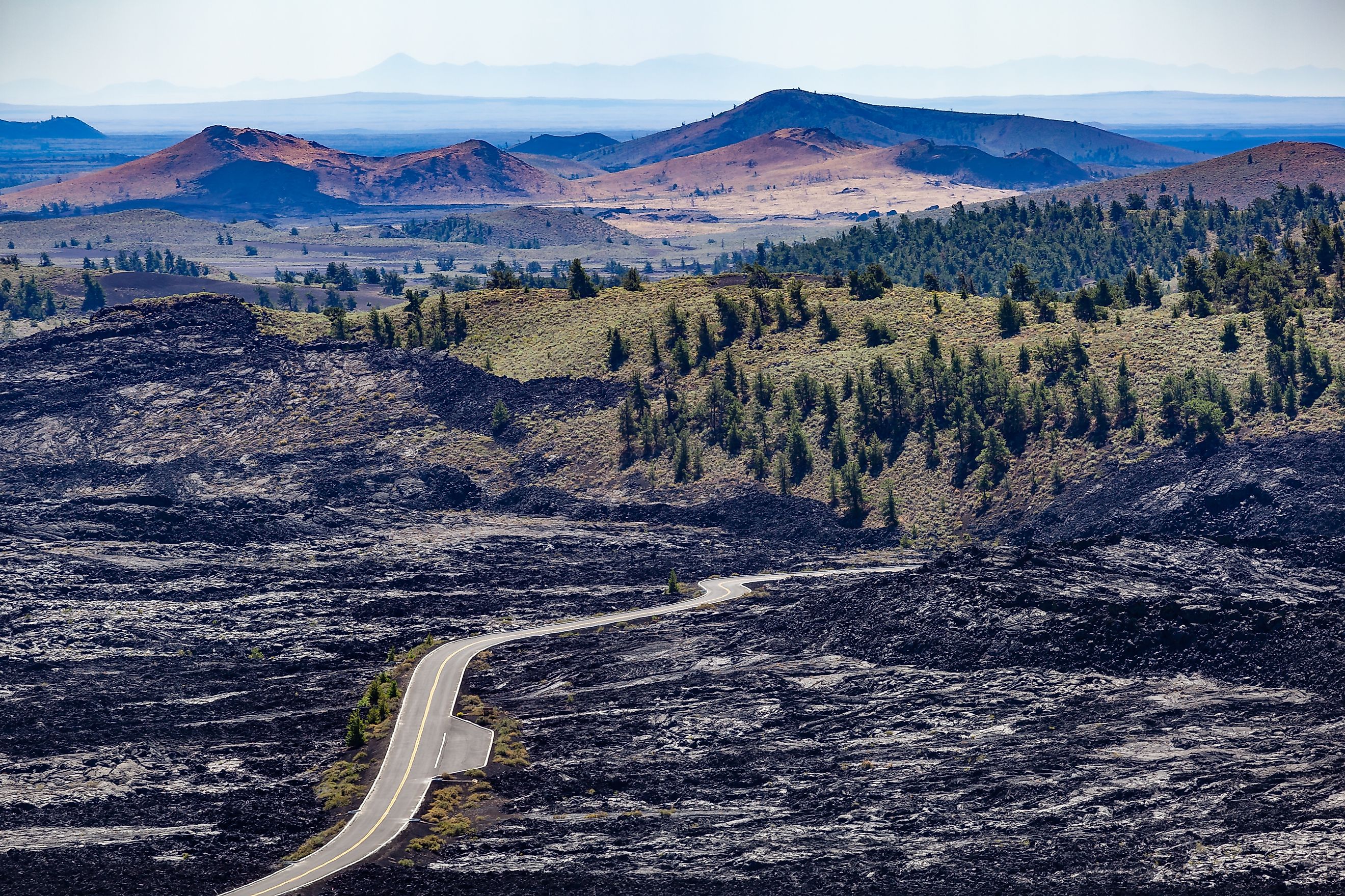 Road that runs between lava rocks and grasslands with pine trees. Craters of the Moon National Monument and Preserve is a United States National Monument and National Preserve on the Snake River Plain