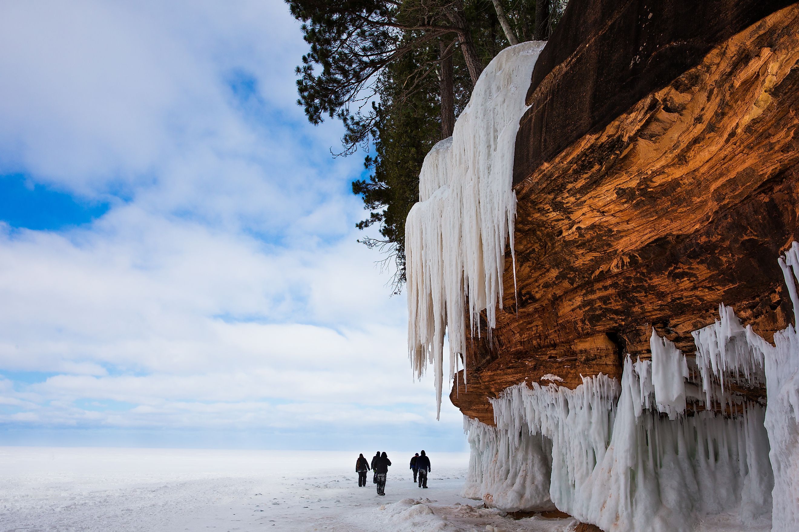 Frozen Lake Superior shoreline. Orange cliff, large icicles and hikers. Apostle Islands National Lakeshore on Lake Superior.