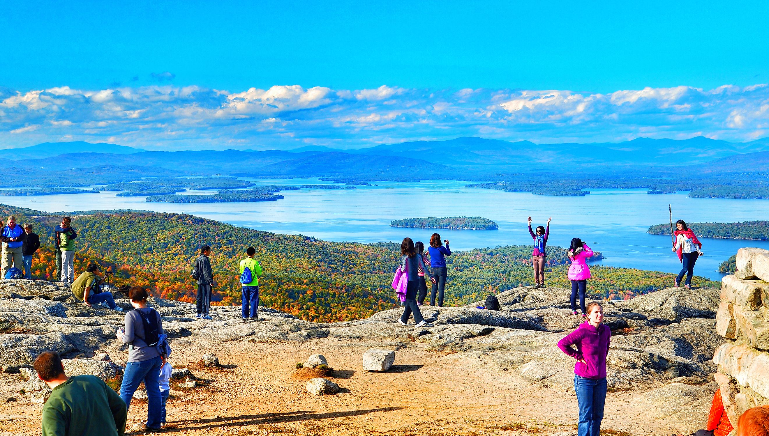Tourists posing for photos at the summit. Lake Winnipesaukee and the Belknap Mountains. Editorial credit: Helioscribe / Shutterstock.com